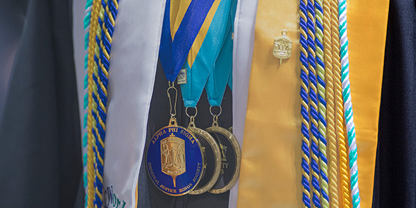 student in graduation gown with medallions and cords