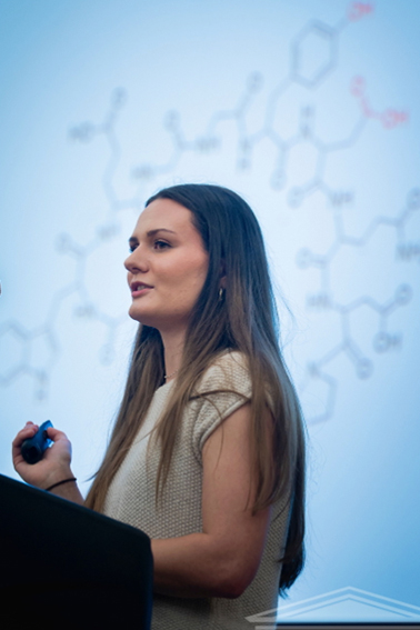 UNCW student with chemistry diagram on screen behind her
