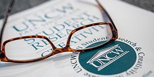 Reading glasses resting on UNCW student research book