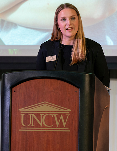 UNCW senior Camille Bayer stands at a podium and speaks at the UNCW Endowed Scholarship Appreciation Dinner.